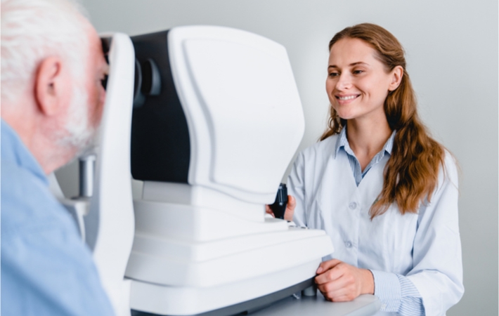 Young smiling female optometrist examines a mature male patient with an autorefractor.