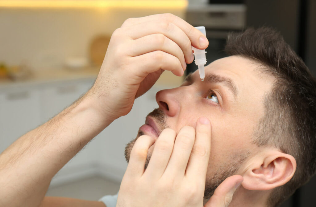 A man putting eye drops into his left eye.