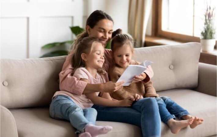 A mid 40s sitting on her couch and reading to her daughters without needing glasses.