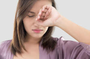 a woman in a purple shirt rubs her eye with her hand