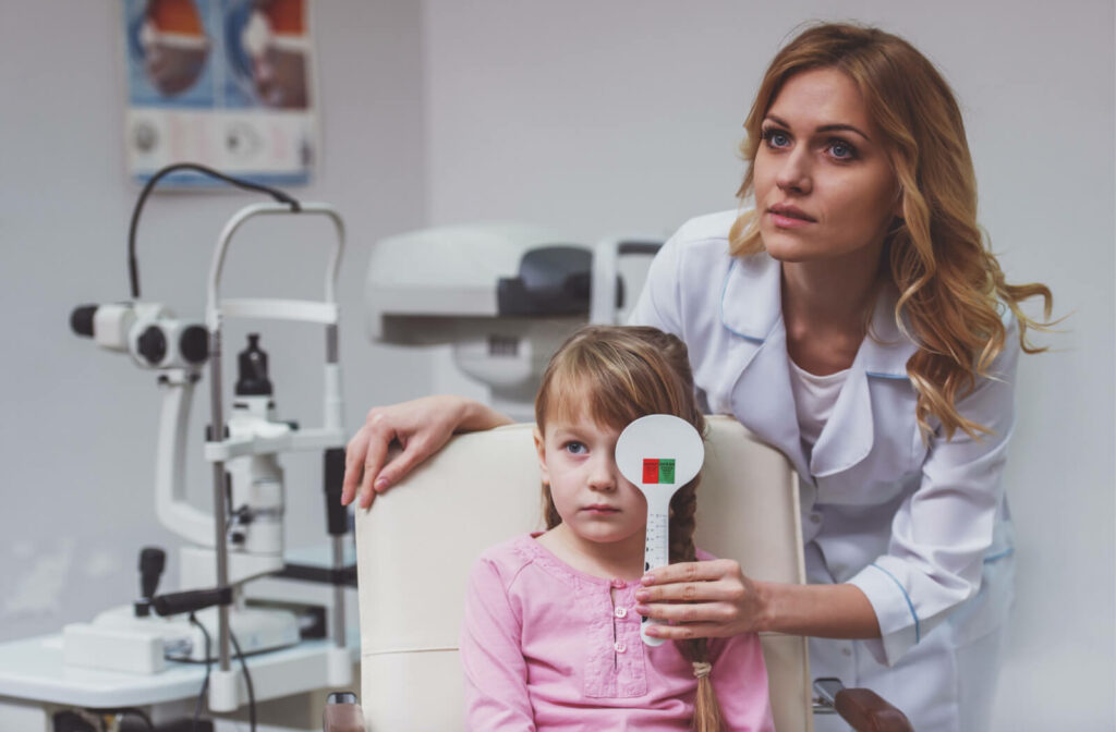 A female optician is covering the left eye of a female child and doing a visual acuity exam.