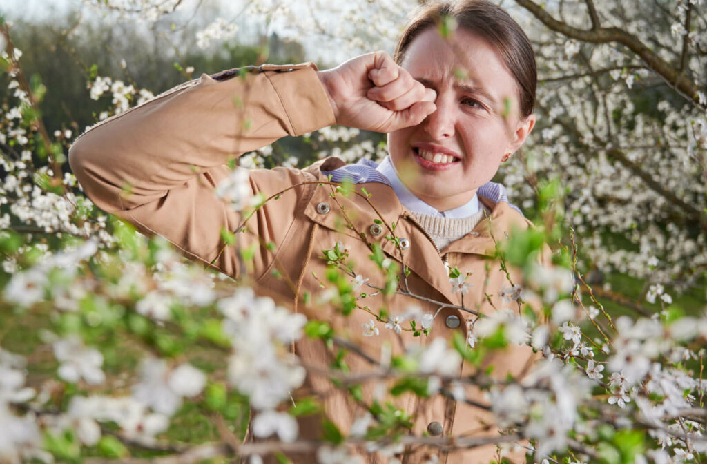 A young woman scratching her itchy eyes due to allergies from the pollen.