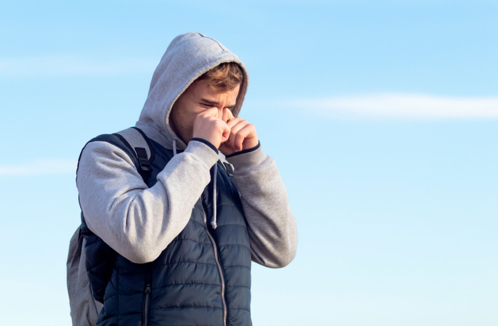 A hooded young man rubbing his eyes due to grittiness.