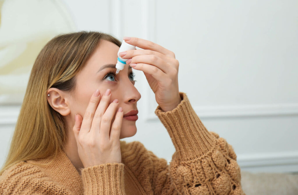 A young woman in a knitted sweater pulling her right eye down so she can properly apply artificial tears. dry eye