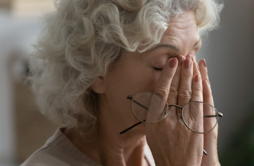 Close-up of a senior woman holding her hands over the bridge of her nose with her eyes closed and her eyeglasses in her right hand