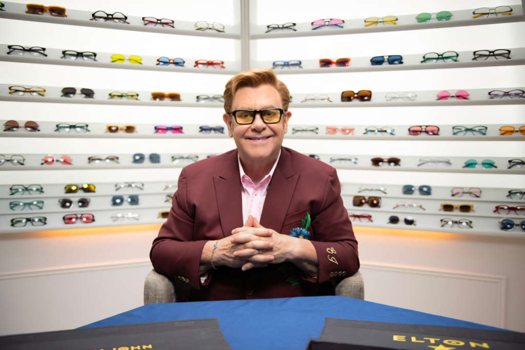 Elton John sitting in front of his large collection of eyewear